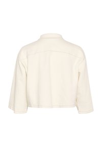 Camicia in cotone color crema, tagliata, con colletto e maniche lunghe. Presenta una cucitura centrale sulla parte superiore della schiena. Texture morbida.