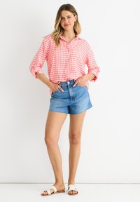 Camicia a quadri rosa e bianca con maniche arrotolate, abbinata a pantaloni corti in denim azzurro e sandali bianchi.