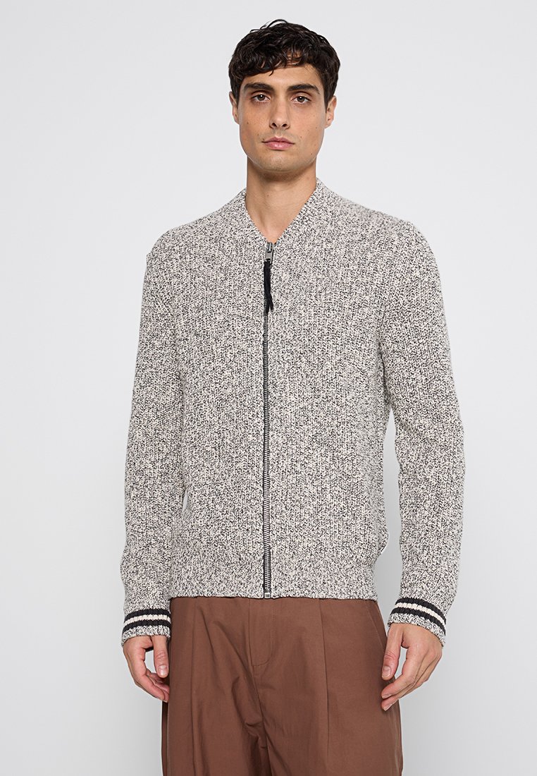 Veste bomber tricotée gris clair avec fermeture éclair sur le devant, tissu texturé et poignets rayés noir et blanc. Elle présente un col montant et des poches.