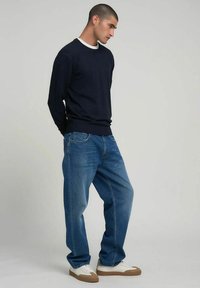Maglione navy lavorato a maglia con scollo bianco, abbinato a jeans blu a gamba larga e sneakers bianche con suole e dettagli beige.