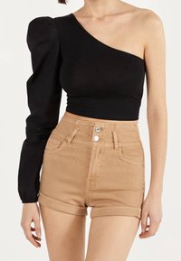 Mustat olkaimettomat yläosat, joissa on pörheä hiha ja tiukka muotoilu, yhdistettynä korkeavyötäröisiin, vaaleanruskeisiin farkkushortseihin, joissa on taitetut lahkeet ja etupainikkeet.