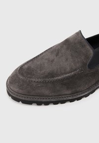 Chaussure à enfiler en daim gris avec une texture lisse, bout arrondi, couture contrastante et semelle en caoutchouc noire dotée de grip antidérapant.