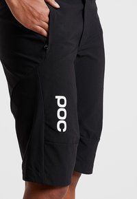 Černé šortky z lehkého materiálu s prostornou kapsou, zúženým střihem a výrazným bílým logem "POC" na boku.
