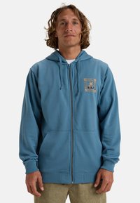 Blue zip-up hoodie made of soft fabric, featuring a kangaroo pocket and a nature-themed logo on the chest. Ribbed cuffs and hem.