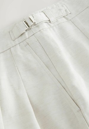 Tissu couleur crème avec une finition texturée, présentant des plis et une fermeture à boucle en argent au niveau de la taille.