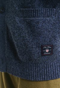 Dunkelblauer, gestrickter Pullover mit einer Tasche, die ein kleines rechteckiges Patch mit der Aufschrift "New Haven Connecticut" und einem Schildemblem in rot, weiß und blau zeigt.