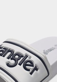 Άσπρο σανδάλι με φάσα, με μαύρο ανάγλυφο λογότυπο Wrangler στη φάσα, με υφή στην σόλα που φαίνεται στο βάθος.