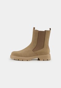 Bottines Chelsea beige en suède lisse, avec des panneaux latéraux élastiques et une semelle en caoutchouc épaisse. Dotées de coutures renforcées et d'une languette.