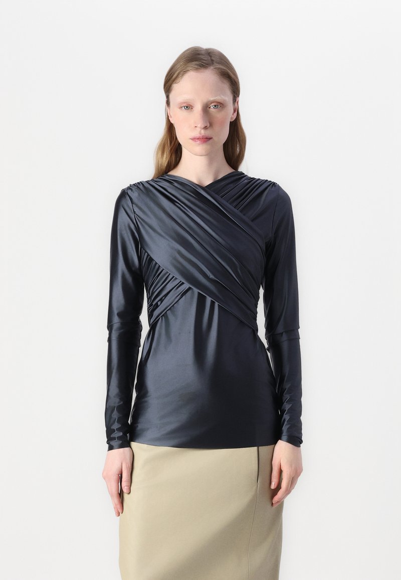 Mørk satengbluse med lange ermer og innviklet design, som har folder og en myk glans. Kombinert med et beige skjørt.