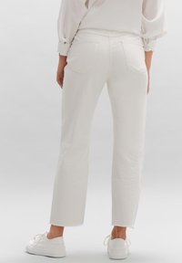 Vaqueros blancos de pierna recta con dobladillo sin rematar y bolsillos traseros, combinados con zapatillas blancas. La tela parece suave y ligera.