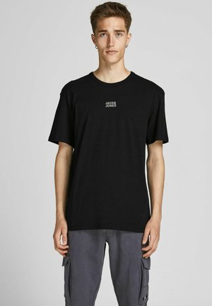 T-shirt en coton noir avec col rond, arborant un petit logo blanc "JACK & JONES" sur la poitrine. Modèle portant un pantalon cargo gris.