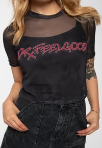 Black cropped mesh top with short sleeves featuring a graphic print "DR. FEELGOOD" in red. Textured material with a semi-sheer design.