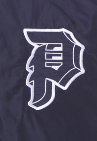 Tissu bleu marine brodé avec un logo "D" stylisé à contour blanc, présentant un design audacieux et angulaire.