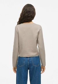 Haut ajusté à manches longues de couleur beige clair, doté d'un col arrondi et d'une texture lisse, associé à un jean en denim bleu taille haute.