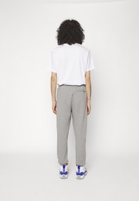 Grå sweatpants med elastisk talje og baglomme, parret med en plain hvid t-shirt og sneakers med blå detaljer.