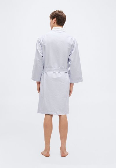 Άνδρας που στέκεται ξυπόλητος, γυρισμένος με την πλάτη, φοράει ρόμπα μέχρι το γόνατο με ανοικτό γαλάζιο και λευκό ριγέ, με μακριά μανίκια και ζώνη.