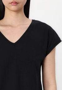 Svart V-ringad t-shirt med korta ärmar, tillverkad av mjukt tyg. Enkel design, slät textur och avslappnad passform. Inga mönster eller detaljer.