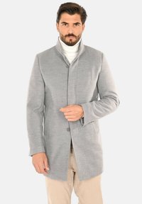 Cappotto di lana grigio chiaro con collo alto, chiusura frontale con bottoni e maniche lunghe. Tessuto liscio, design minimalista e tasche laterali.