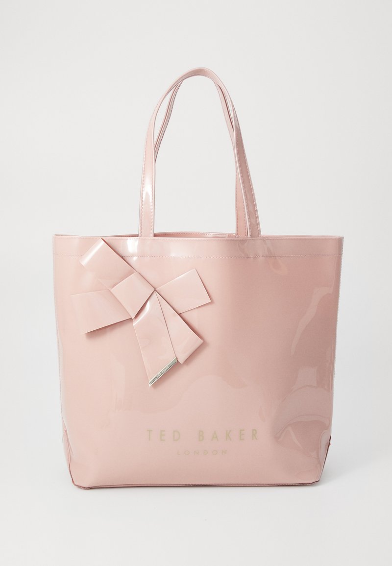 Rosa glansig tote-väska tillverkad av lackat material, med en stor rosettdetalj på framsidan och märkesnamnet "TED BAKER LONDON" tryckt i guld.