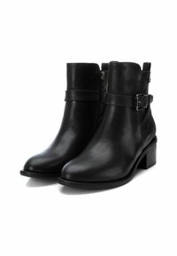 Botas de cuero negro hasta el tobillo con un ligero tacón, con cremallera lateral y una correa ajustable con detalle de hebilla metálica.