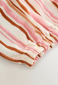 Tissu à rayures horizontales roses, marron et blanches, avec un détail de poignet élastique froncé sur un fond clair.