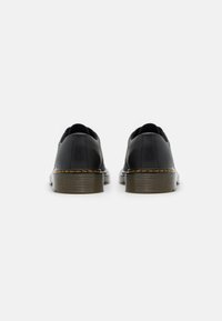 Scarpe nere in pelle con punta tondeggiante e lati elasticizzati. Presentano una suola marrone texturizzata con cuciture gialle. Design minimalista.