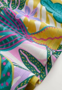 Bunt gewebter Stoff mit großen tropischen Blättern in Grün, Gelb und Pink, mit weicher Textur und filigranen Stickdetails.