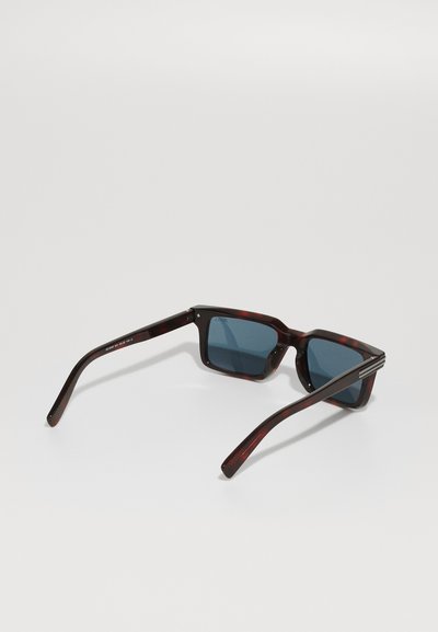 Sunglasses with a dark tortoiseshell frame, blue lenses, square shape, and thick, glossy temples featuring subtle metal accents.