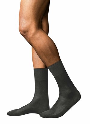 Calcetines de algodón negros con una textura suave, puños acanalados y una longitud a media pantorrilla, mostrados en una pierna parcialmente visible.