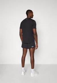 Black short-sleeve athletic shirt with smooth texture and logo on the back, paired with black shorts featuring a white logo at the hem.