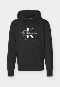 Crna dukserica od pamuka, s prednjim džepom, podesivim šnselama i bijelim Calvin Klein Jeans logotipom preko grudi.