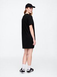 Robe T-shirt noire avec une coupe décontractée, des manches courtes et un col rond, associée à une casquette noire et des baskets noires. Design épuré.
