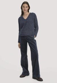 Navy-blauer gerippter Strickpullover mit V-Ausschnitt und langen Ärmeln, kombiniert mit weit geschnittenen Navy-Cordhosen. Glatte Textur mit lockerer Passform.