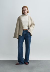 Μπεζ oversized σακάκι πάνω από λευκό ζιβάγκο, συνδυασμένο με μπλε τζιν φαρδιάς γραμμής και καφέ παπούτσια. Λείο ύφασμα και άνετη εφαρμογή.