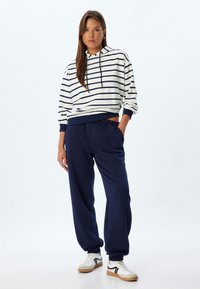 Hvid og marineblå stribet hættetrøje med snoretræk, parret med marineblå sweatpants. Begge er i afslappede fit stoffer. Casual sneakers fuldender looket.