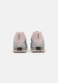 Zapatillas deportivas en gris y rosa que presentan una parte superior suave, un cuello acolchado y una doble amortiguación en el talón. Detalles perforados para mayor transpirabilidad.