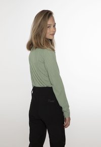 Top verde a maniche lunghe con coste, caratterizzato da una finitura testurizzata, abbinato a pantaloni neri a vita alta. I pantaloni presentano dettagli ricamati sul retro.