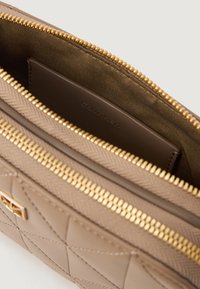 Calvin Klein beige quiltet toilettaske med en guld lynlås, glat indvendig foering og et synligt brandlogo på en brun kortholder.