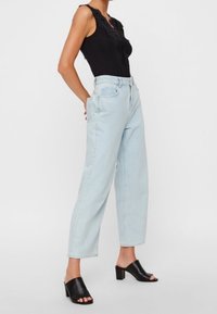 Body in pizzo nero con bordatura, jeans a vita alta azzurri e mule neri con tacco a blocco e punta aperta. Design semplice con una vestibilità rilassata.