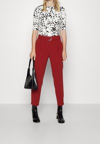 Black and white speckled top paired with high-waisted red trousers, a black croc-embossed handbag, and black ankle boots.