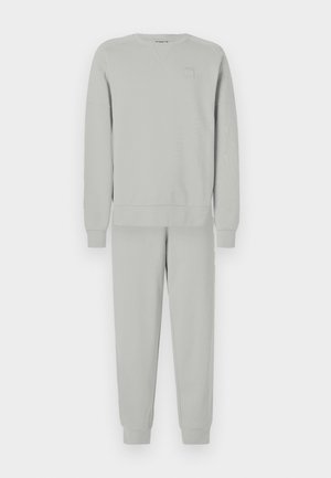 Světle šedý svetr a odpovídající souprava tepláků. Měkká tkanina s žebrovanými manžetami a lemem, na hrudi svetru je malé logo.