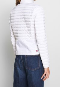 Vit pufferjacka med hög krage, quiltad yta och en synlig logotypdetalj. Matchad med mörkblå denim, som visar en strömlinjeformad design.