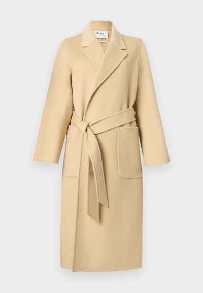 Μπεζ μακρύ μάλλινο παλτό με φαρδιές πέτρες, ζώνη δέσιμου στο χρώμα του παλτού, δύο εμπρόσθιες τσέπες και μακριά μανίκια.