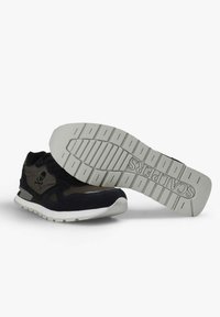 Zapatilla negra y gris con suela blanca, un zapato mostrando el lateral con el logo de una calavera, el otro mostrando la suela con el branding "SCALPERS".