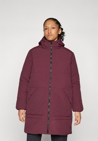 Manteau matelassé bordeaux avec un col haut, une fermeture éclair à l'avant, deux grandes poches frontales et des poignets froncés. Texture lisse avec des détails cousus.
