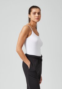 Witte tanktop met dunne bandjes, gecombineerd met zwarte sweatpants met een trekkoord in de taille en zijzakken. Glad, aansluitend materiaal.