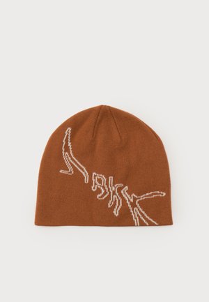 Brun strikket hue med hvidt abstrakt lineært design på forsiden mod en ensartet lys baggrund.