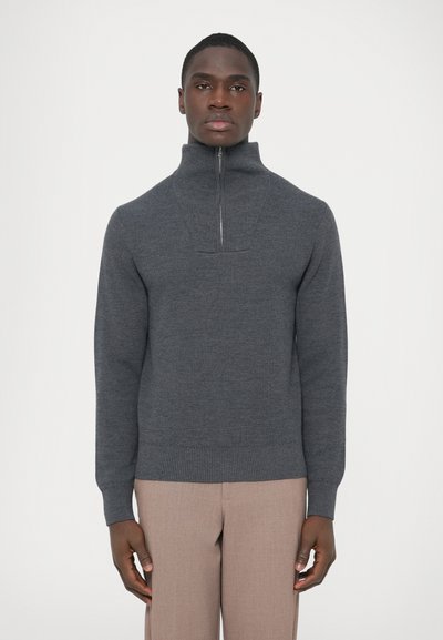 Gray knitted pullover with a high collar, quarter-zip front, ribbed cuffs, and waistband. Smooth texture, slim fit. Paired with light-colored trousers.