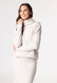 Light beige turtleneck sweater with a textured grid pattern and ribbed cuffs, paired with a matching pencil skirt in the same fabric.