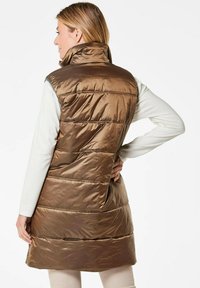 Braune Pufferweste mit hohem Kragen und horizontal gestepptem Muster, ausgestattet mit einer glänzenden, glatten Textur und einem mittellangen Design.